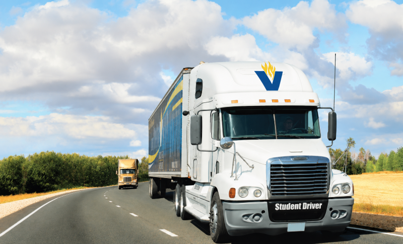 A white semi-truck featuring the Vincennes University logo and a "Student Driver" label drives along a winding two-lane road.
