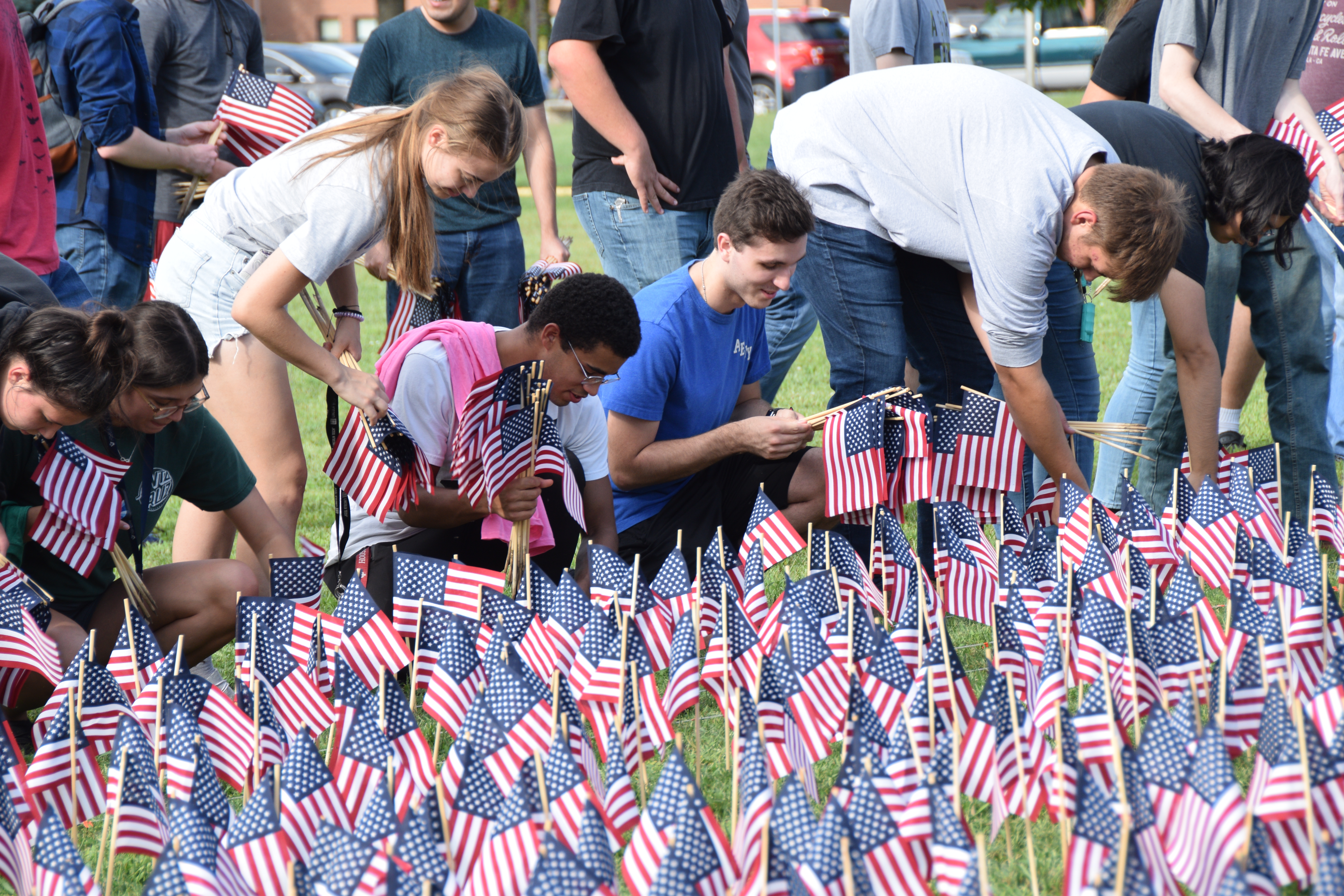 Students placing small American flags in the grass to create a 9/11 flag memorial.