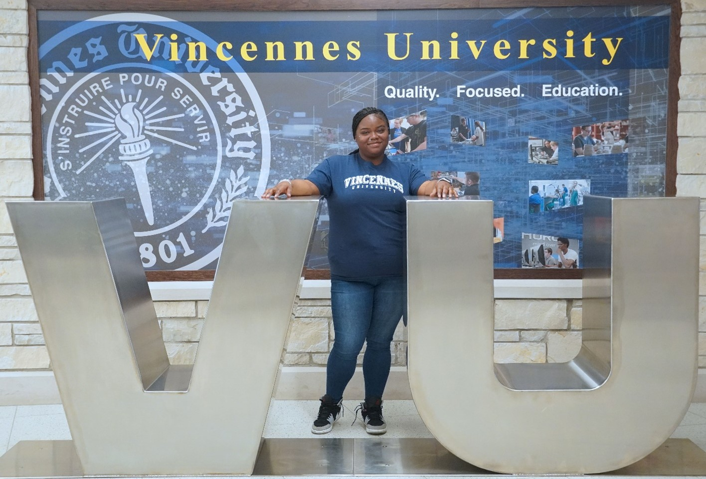 Hannah Jones wearing a VU shirt standing between a large V and large U in the lobby of the Learning Resource Center